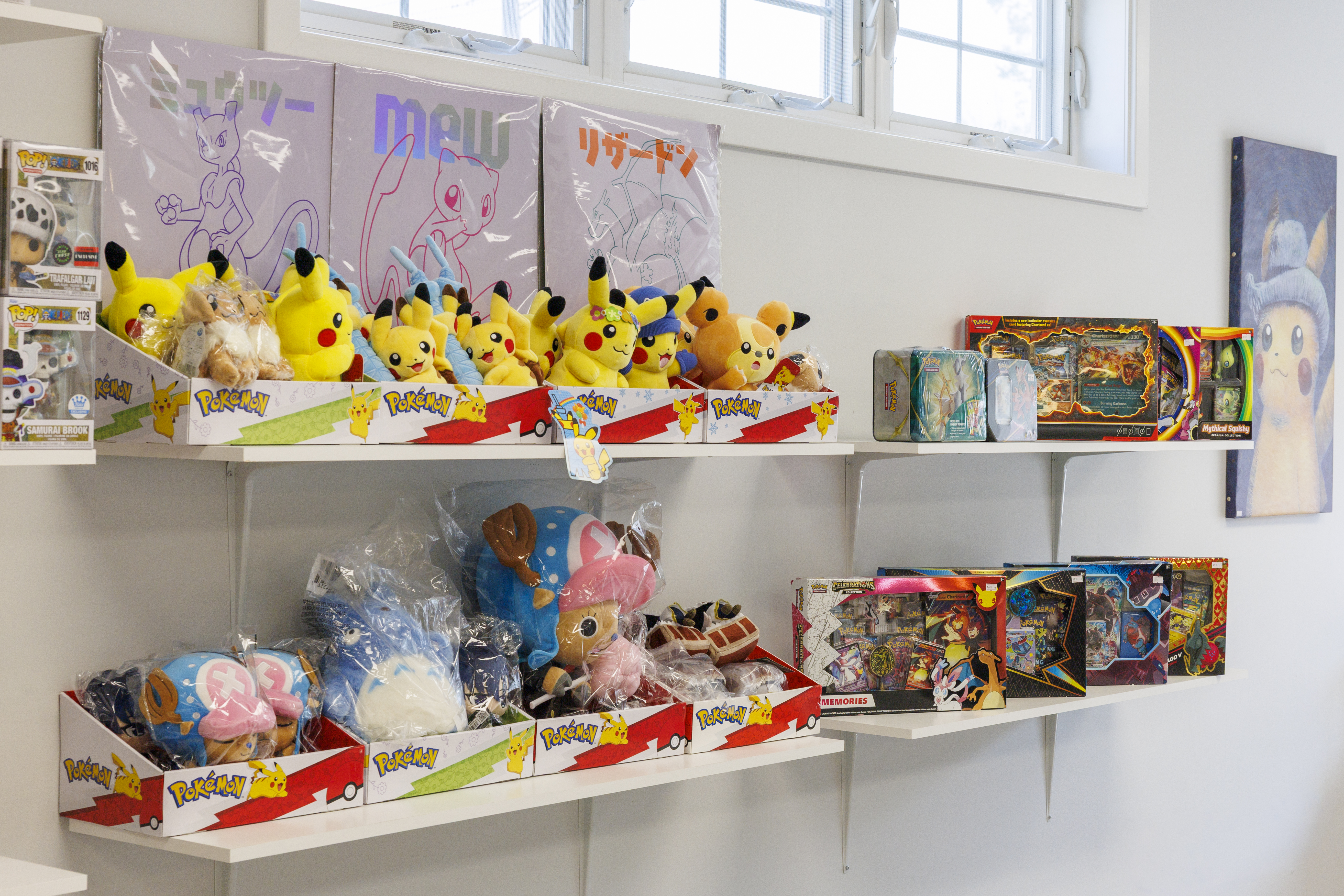 Wall shelves stocked with Pokémon and One Piece plushies, Celebrations collection boxes, and a Pikachu canvas on the wall.